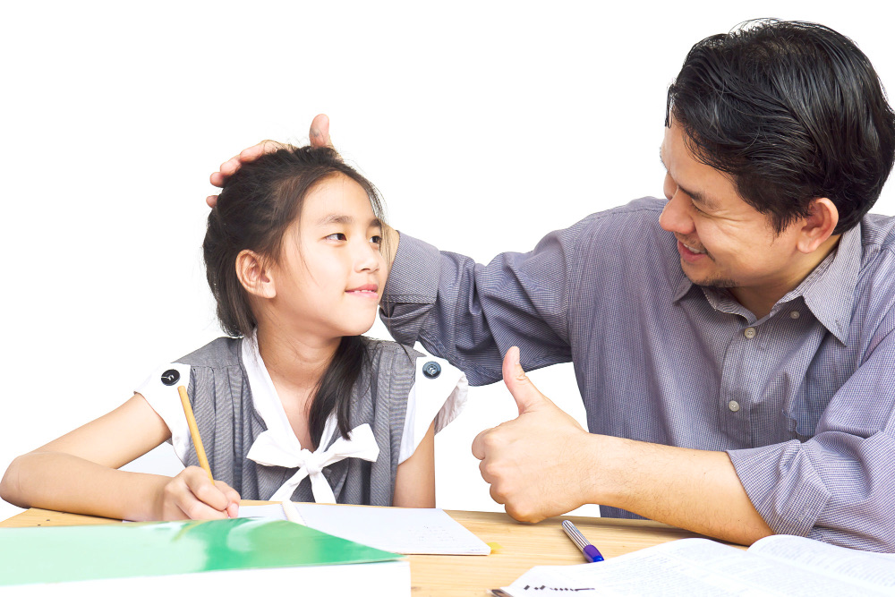 父親以鼓勵的手勢稱讚正在寫作業的女兒,展現正向管教中溫和支持的親子互動